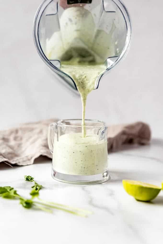 Cilantro lime dressing being poured from a pitcher to a serving container.