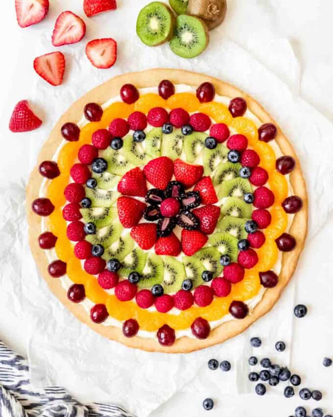 An image of a fruit pizza decorated with fresh kiwi, raspberries, strawberries, grapes, blueberries, and mandarin oranges.