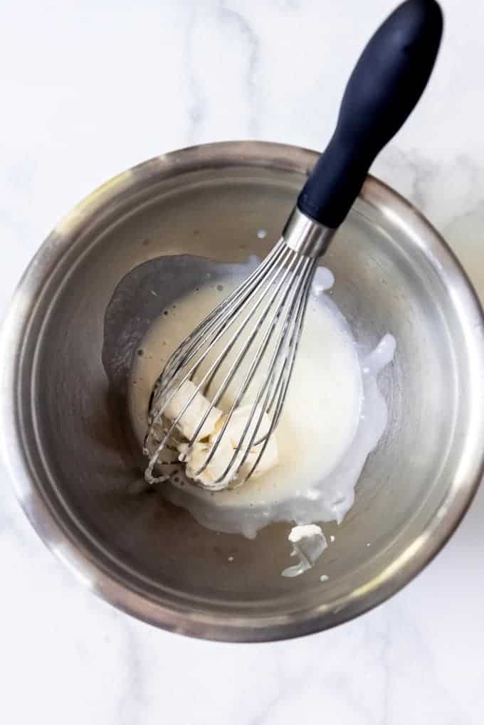 An image of hot cream mixture being added to cream cheese to make an ice cream base.