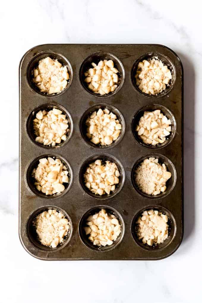 An image of chopped macadamia nuts in the cups of a muffin pan.