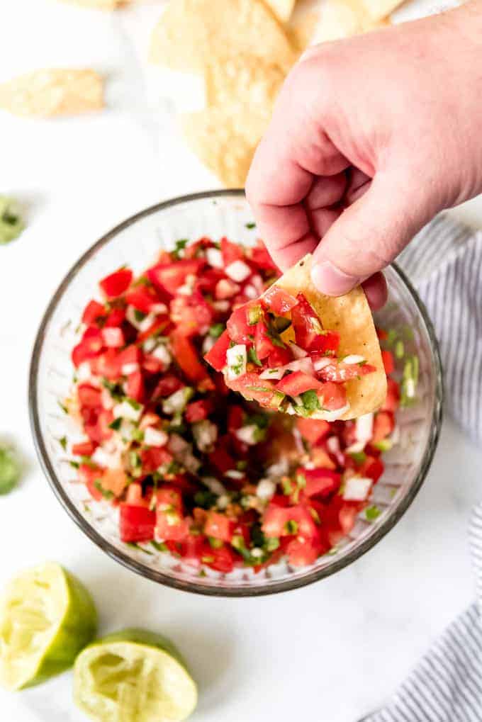 An image of a hand scooping up pico de gallo with a tortilla chip.