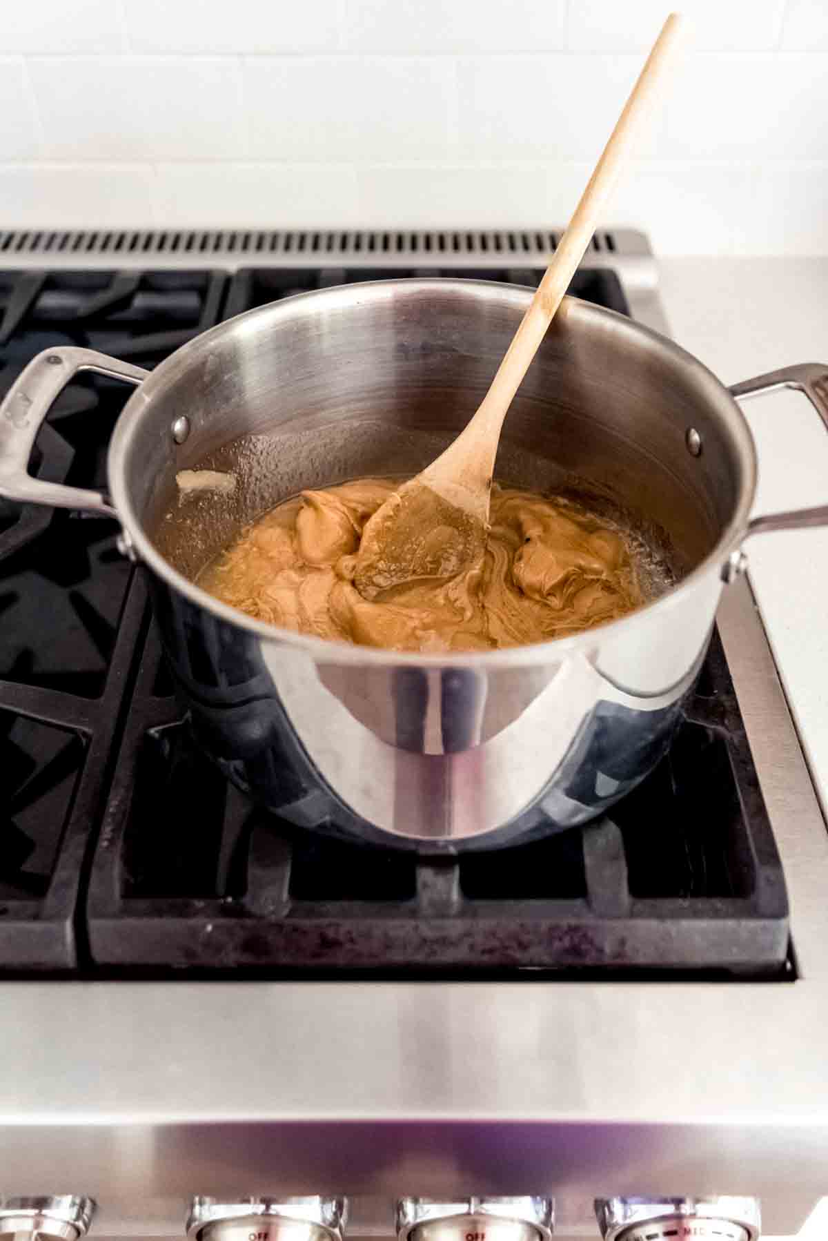 Combining scotcheroo ingredients in a saucepan on the stovetop with a wooden spoon.