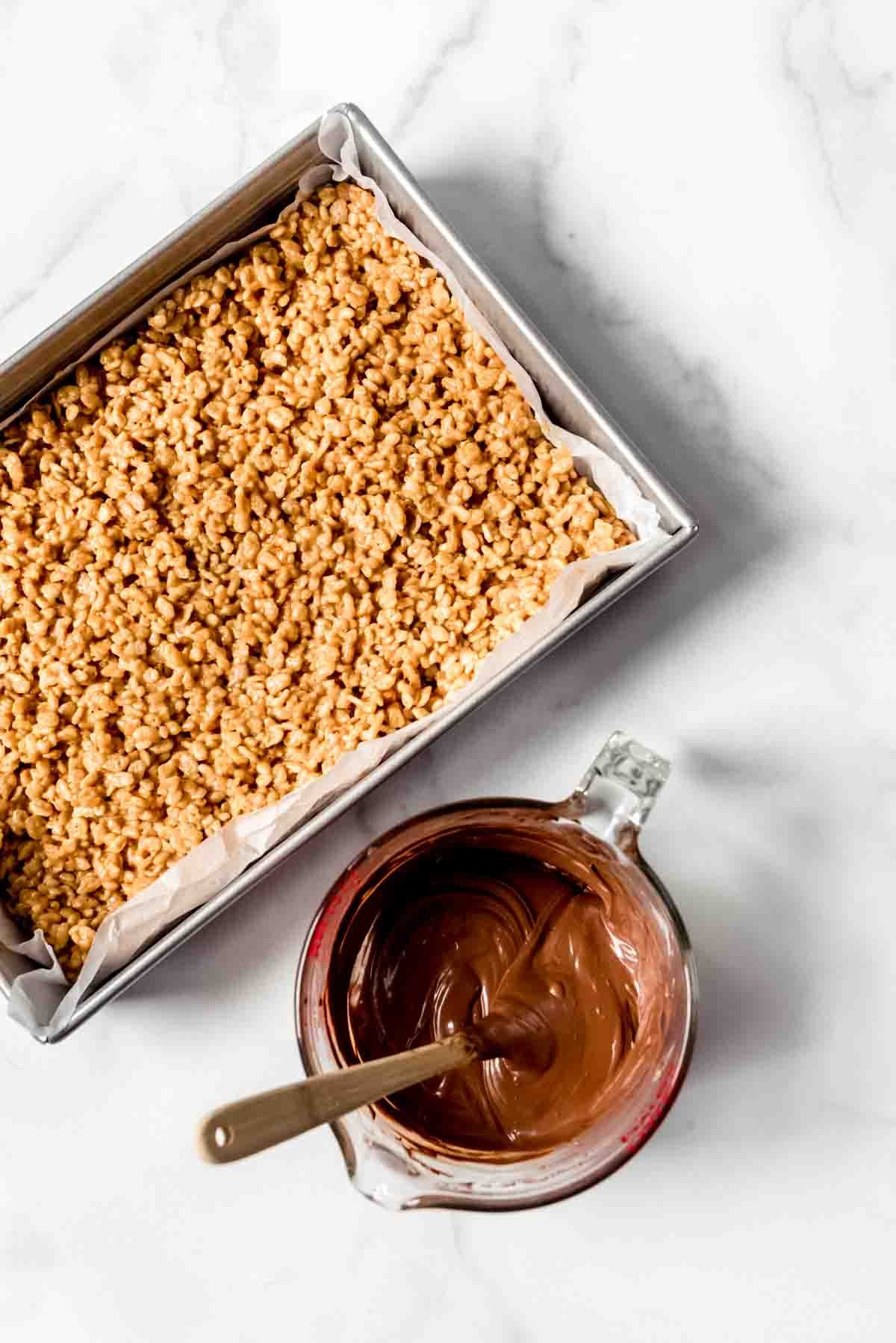 An image of a pan of chewy peanut butter rice krispie treats with melted chocolate next to it for pouring on top.