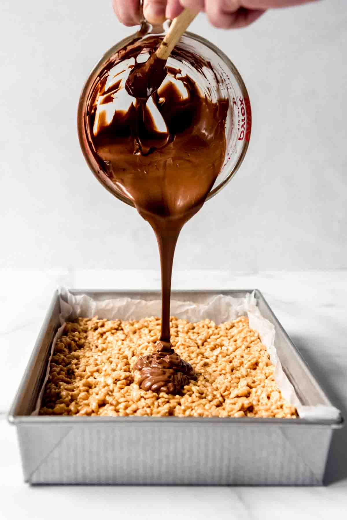 An image of melted chocolate and butterscotch chips being poured over scotcheroos in a pan.