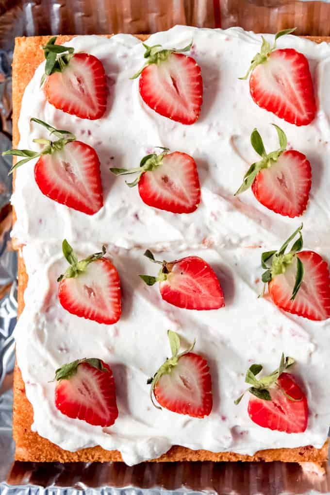 An image of sliced strawberries on top of light whipped cream frosting on a strawberry cake.