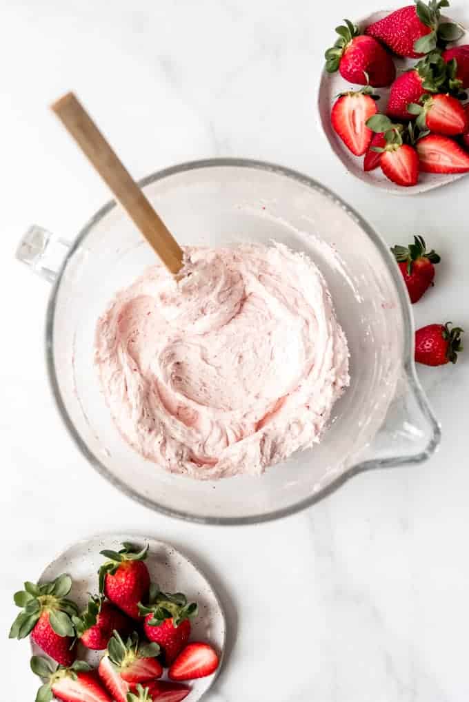 An image of a bowl of homemade strawberry frosting next to a plate of fresh berries.