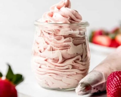 An image of strawberry frosting in a glass jar next to a piping bag with a decorative tip.