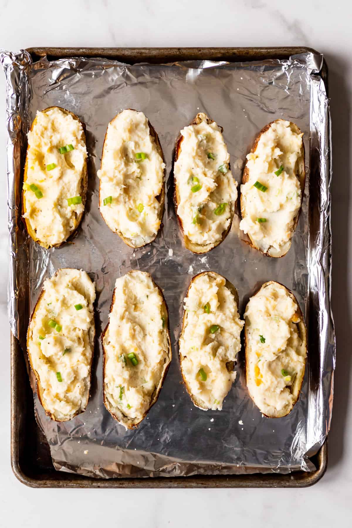 An image of potato skins filled with mashed potatoes, cheese, and green onions.