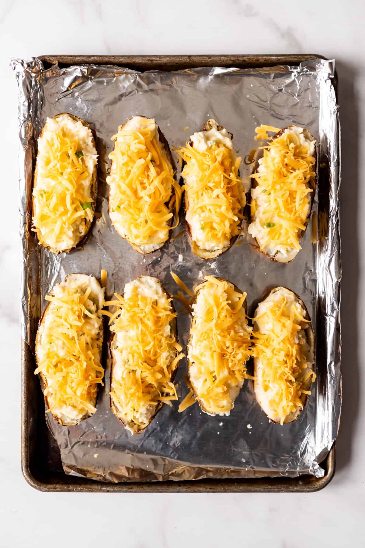 An image of twice baked potatoes covered in cheese and ready to go into the oven.