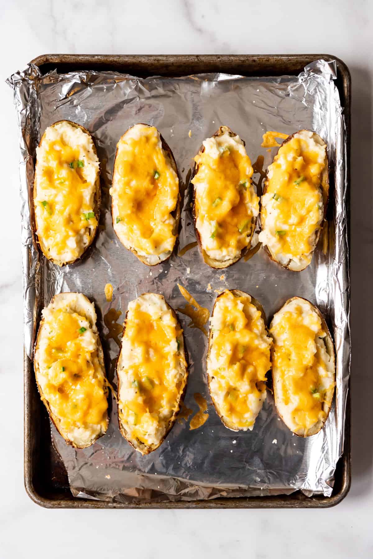 Twice baked potatoes on a baking sheet lined with aluminum foil.