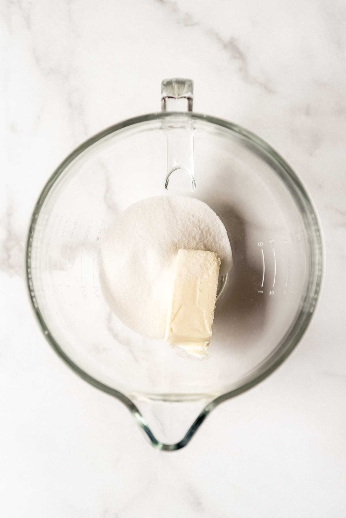 Combining sugar and butter in a glass mixing bowl.