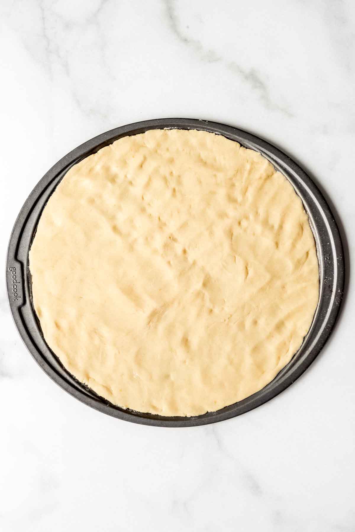 Pressing sugar cookie dough into a pizza pan.