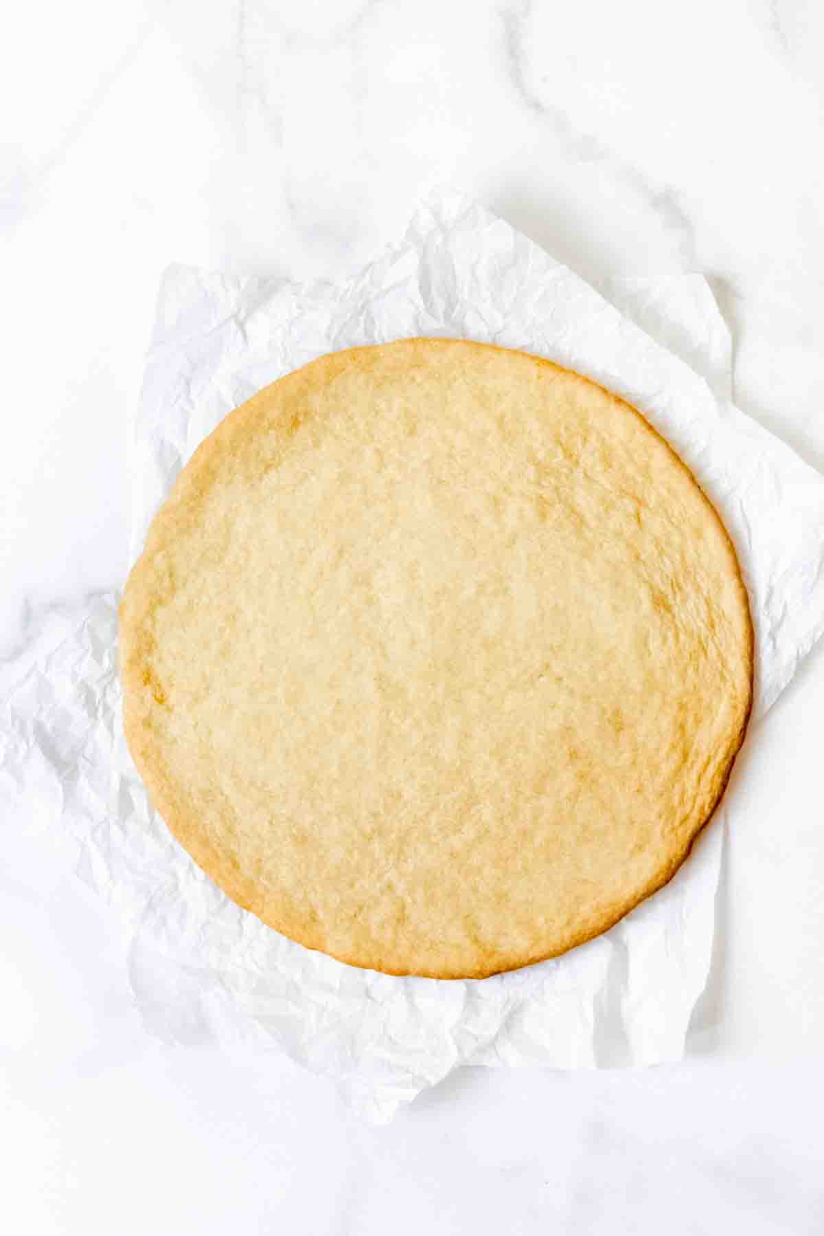 A baked sugar cookie pizza crust on parchment paper.