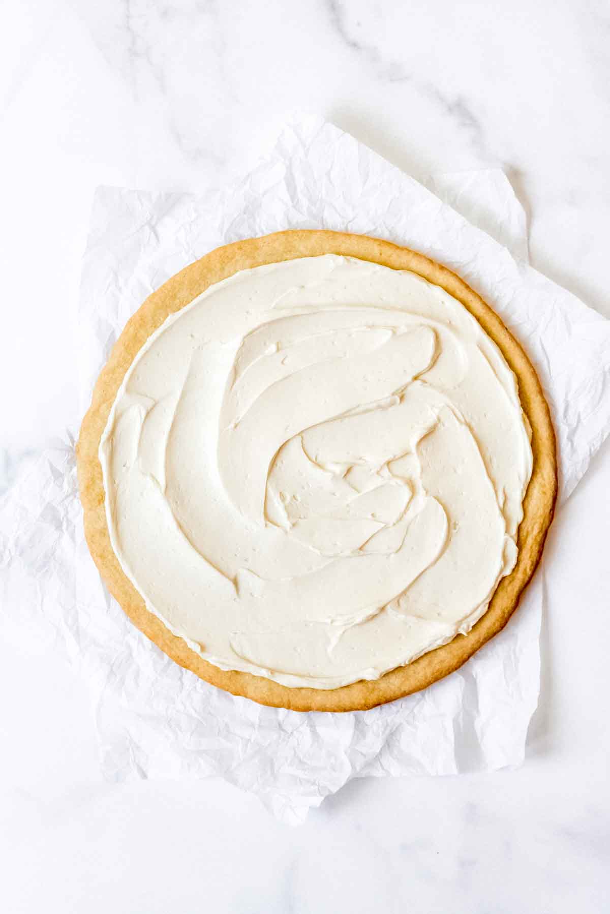 Spreading cream cheese frosting on a sugar cookie pizza crust.