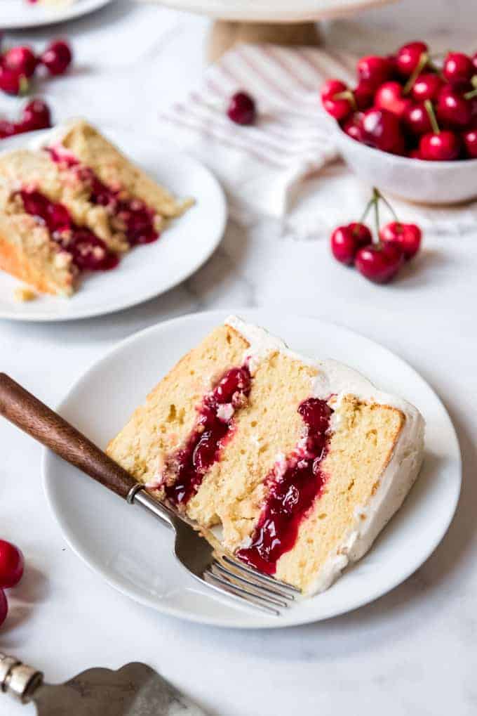 Slices of yellow cake filled with cherry filling on white plates.