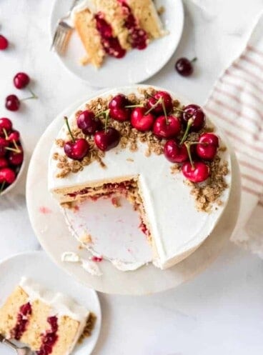 An aerial view of a cake topped with cherries and oatmeal crisp with slices cut out of it.