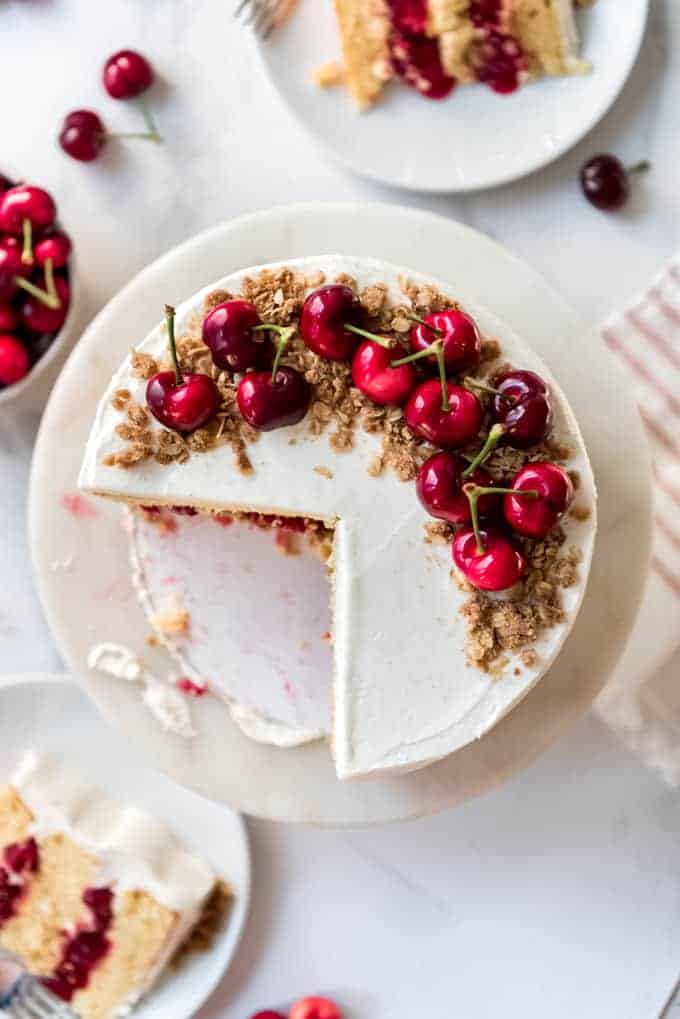 A cake topped with cherries and oatmeal crisp with slices cut out of it.