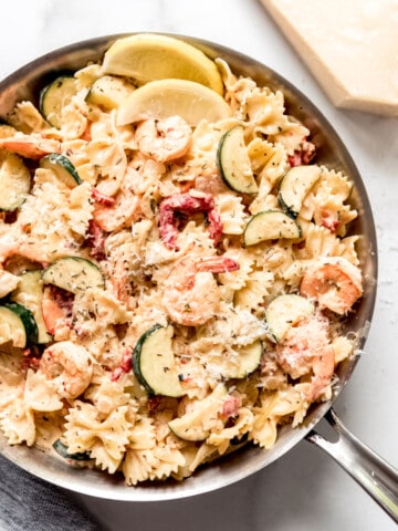A pan of pasta and shrimp with vegetables in a garlic cream sauce.