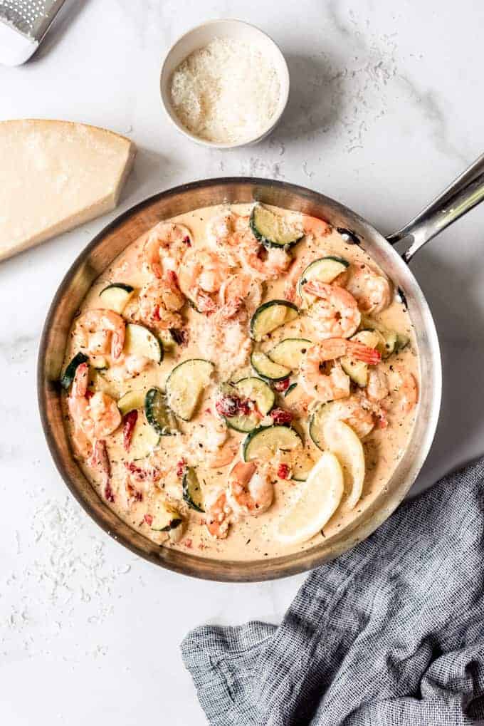 A large pan filled with shrimp and vegetables in a garlic cream sauce next to parmesan cheese.
