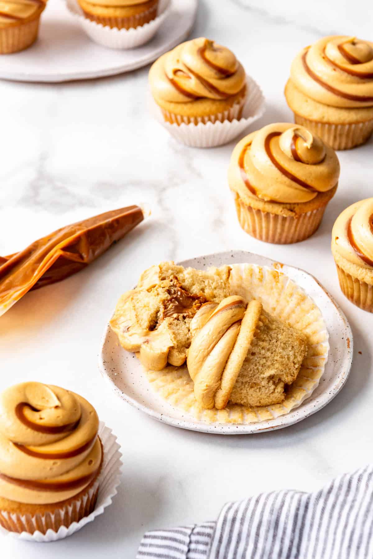 A cupcake that is sliced in half laying on a plate next to more cupcakes with swirled frosting.