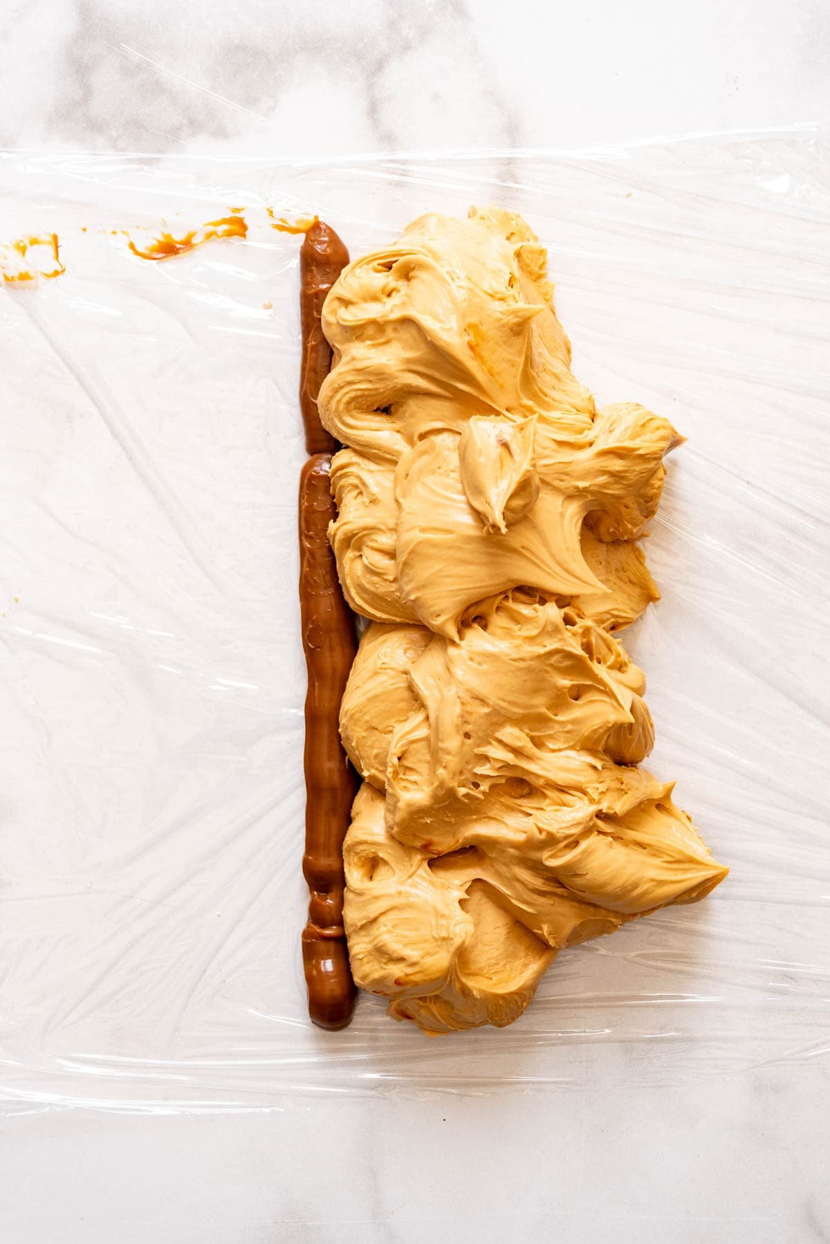 A piece of plastic wrap with a line of dulce de leche piped onto it next to a pile of dulce de leche frosting.