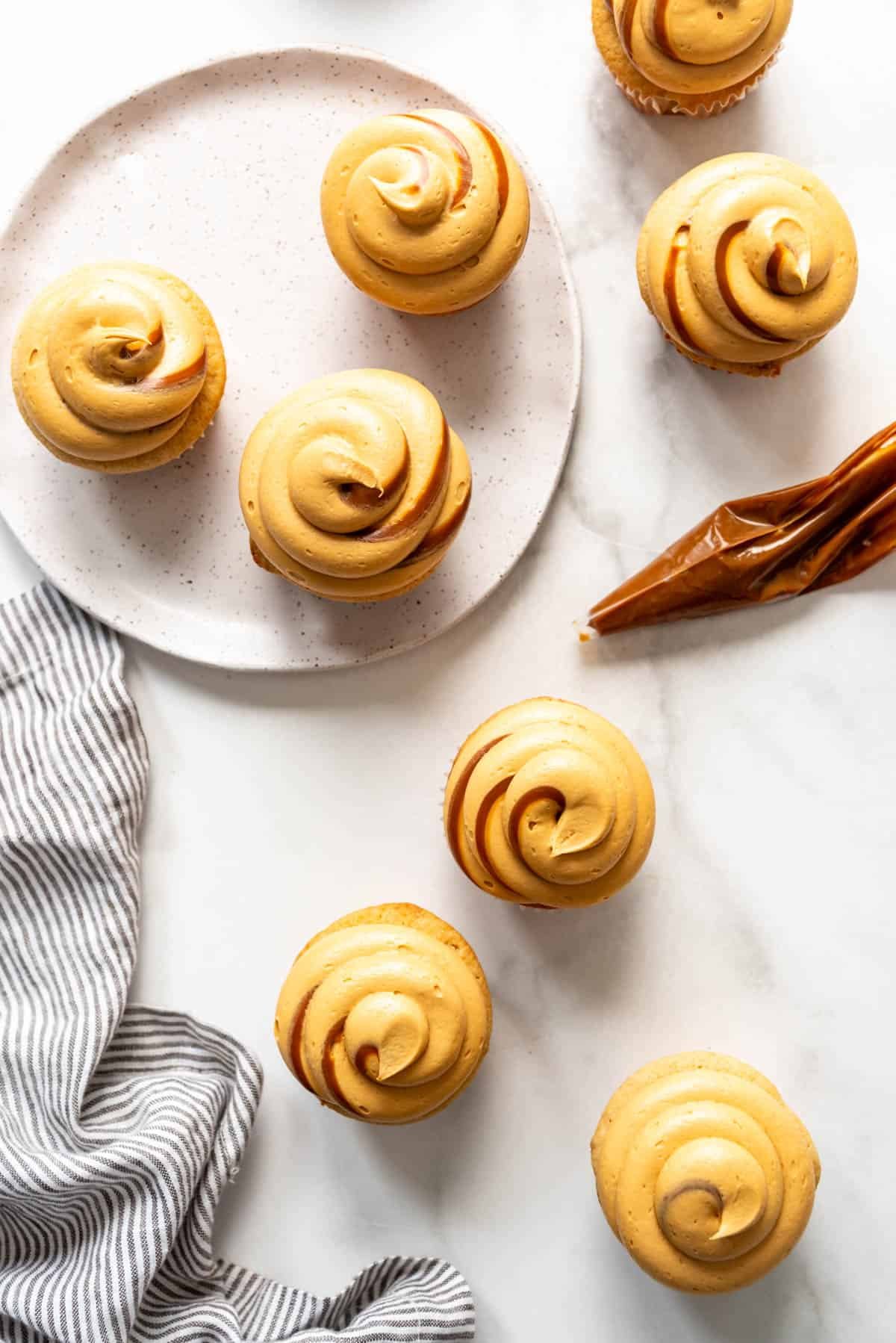 An overheard image of cupcakes with dulce de leche frosting swirled on top, next to a napkin and a piping bag with dulce de leche in it.