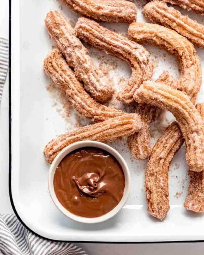 Homemade churros piled in a serving dish with Nutella for dipping.