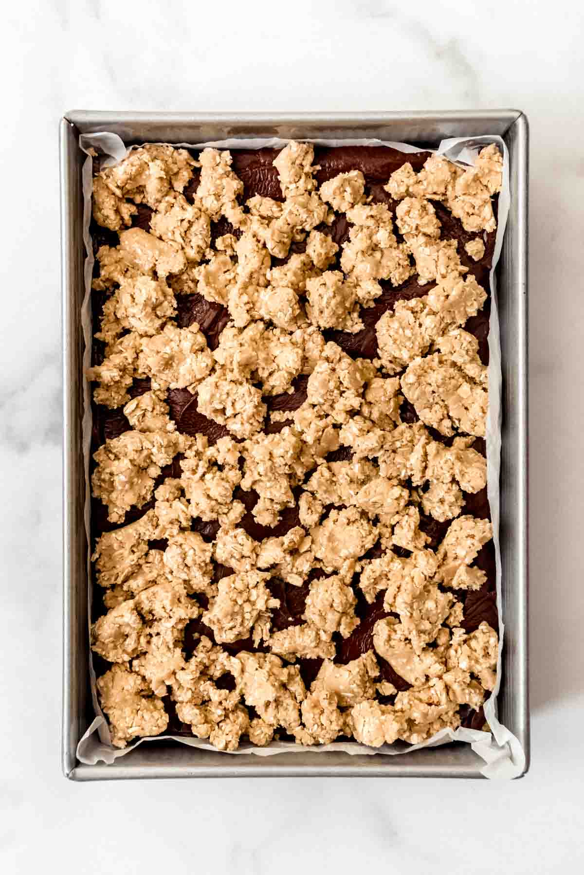 Adding a top layer of oatmeal cookie dough sprinkled over fudge in a 9x13-inch pan.