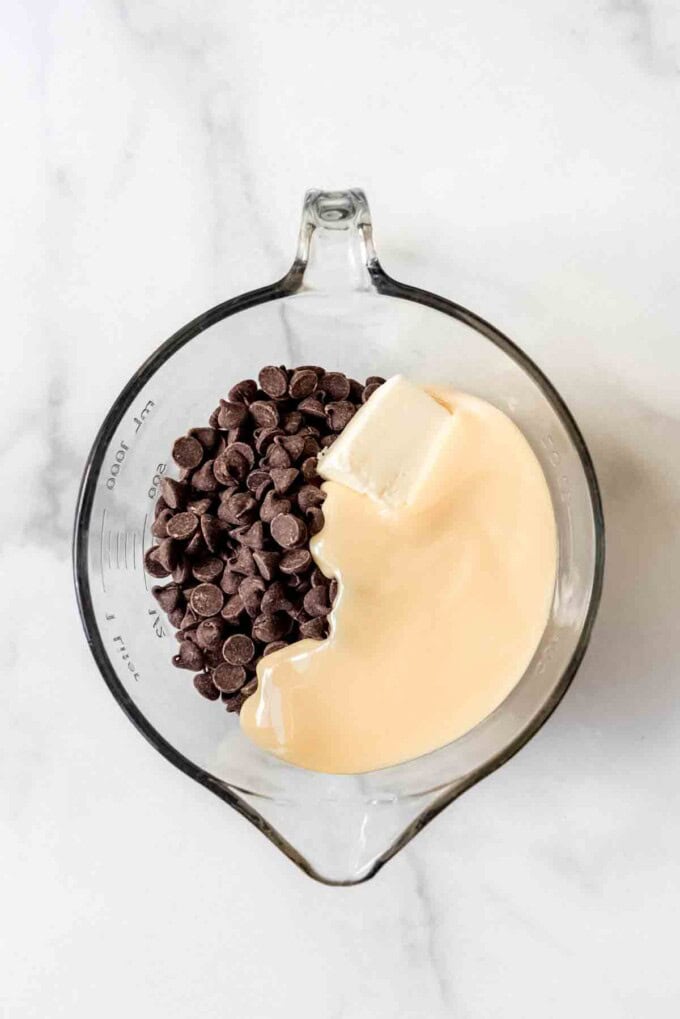 Combining chocolate chips, sweetened condensed milk, and butter in a glass mixing bowl.