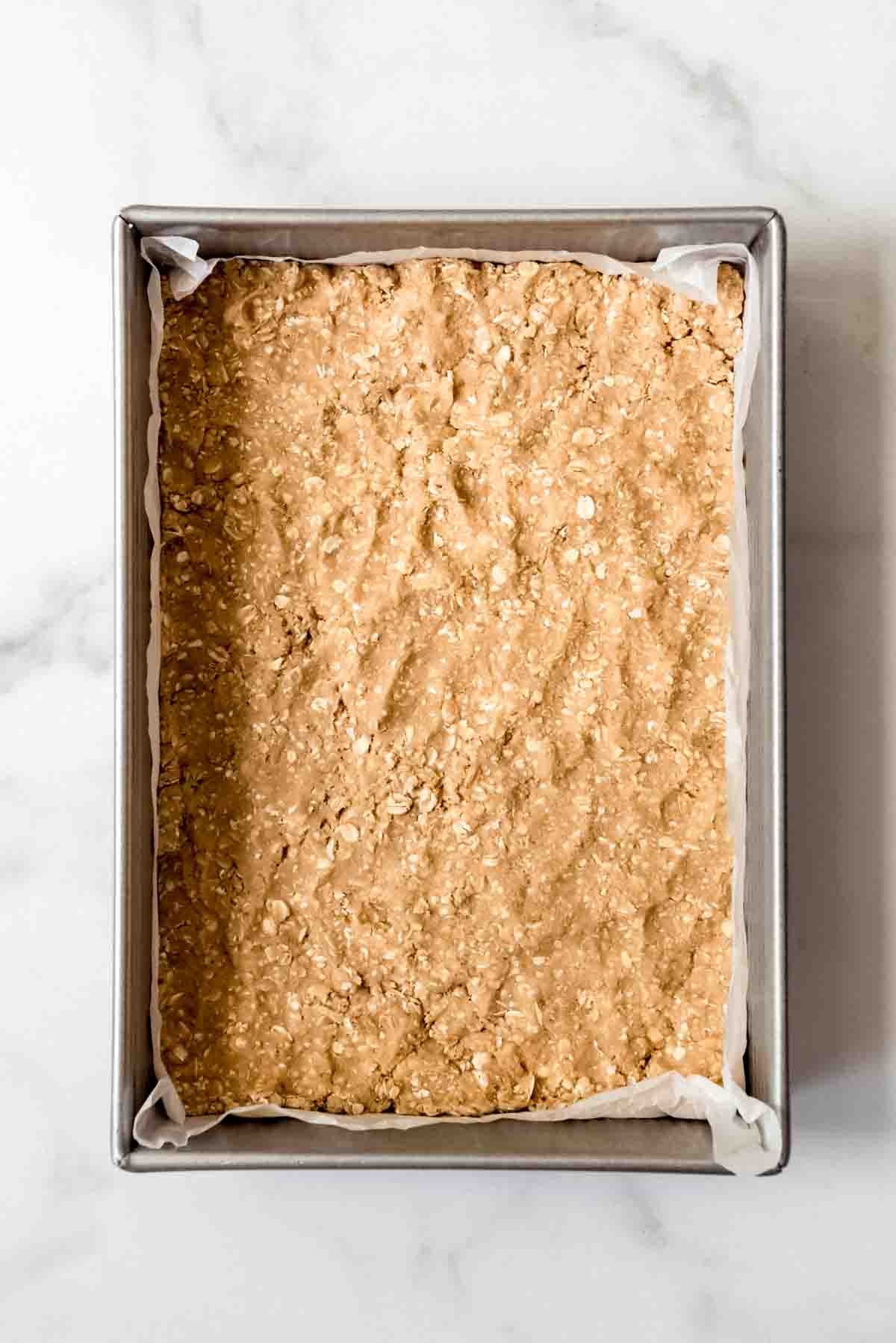 An overhead image of a baking pan with oatmeal cookie dough pressed into the pan.