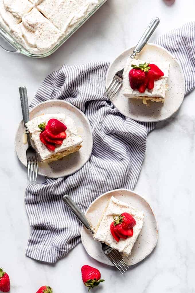 serving plates with slices of tres leches cake, forks, and strawberries on each