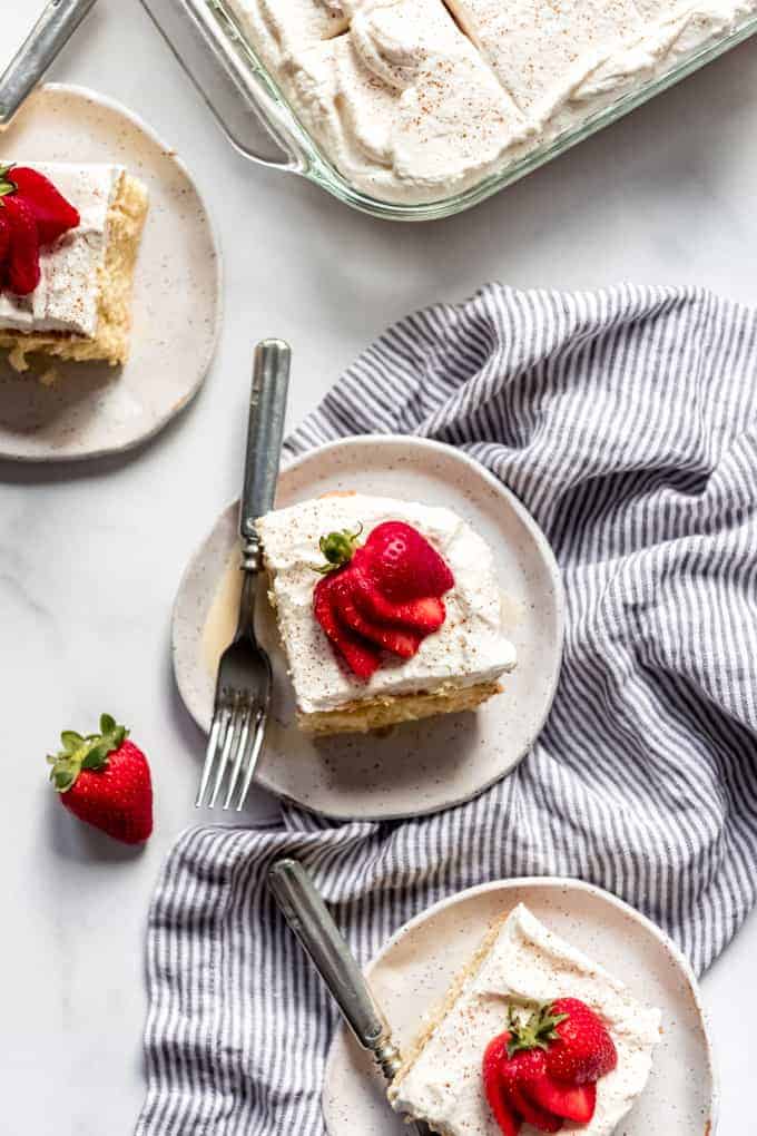 an aerial view of sliced tres leches cake on white plates with strawberries and in a baking dish