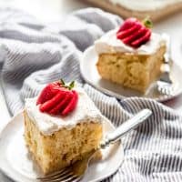 two slices of tres leches cake on serving plates with forks and topped with fanned strawberries