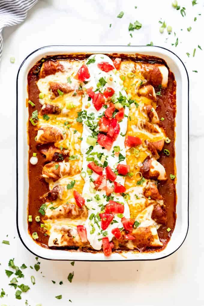 A baking dish full of homemade beef enchiladas topped with sour cream, cilantro, and tomatoes.
