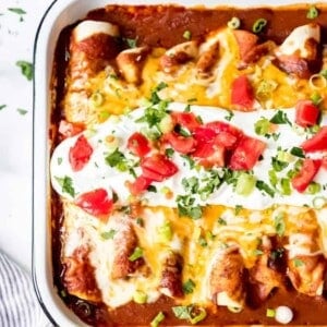 A white baking dish with beef enchiladas inside and garnished with sour cream and extra toppings