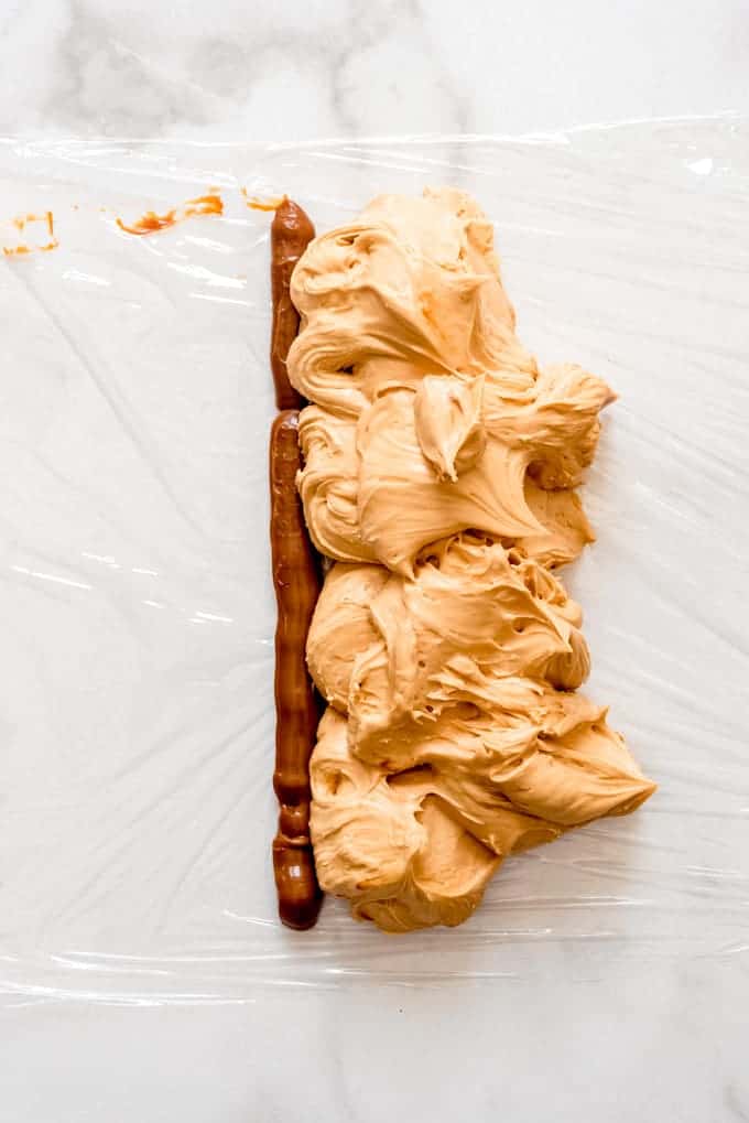 A piece of plastic wrap with a line of dulce de leche piped onto it next to a pile of dulce de leche frosting.