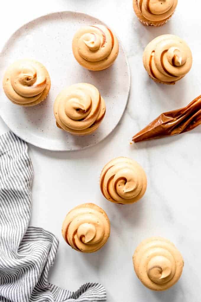 An overheard image of cupcakes with dulce de leche frosting swirled on top, next to a napkin and a piping bag with dulce de leche in it.