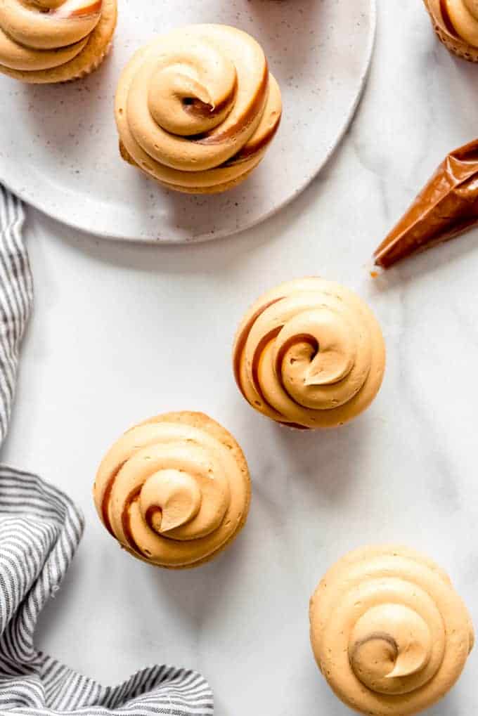Swirls of dulce de leche buttercream frosting on top of cupcakes next to a striped napkin and a plate.