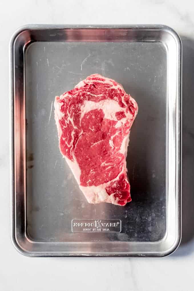 A raw ribeye steak on a metal baking sheet.