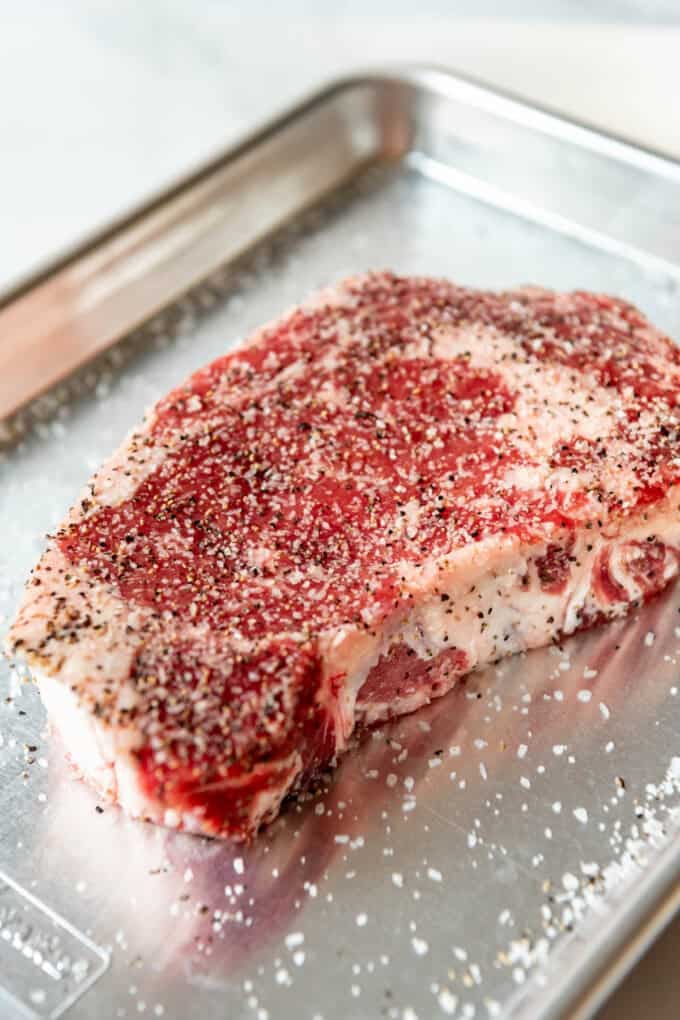 A seasoned ribeye steak on a baking sheet.