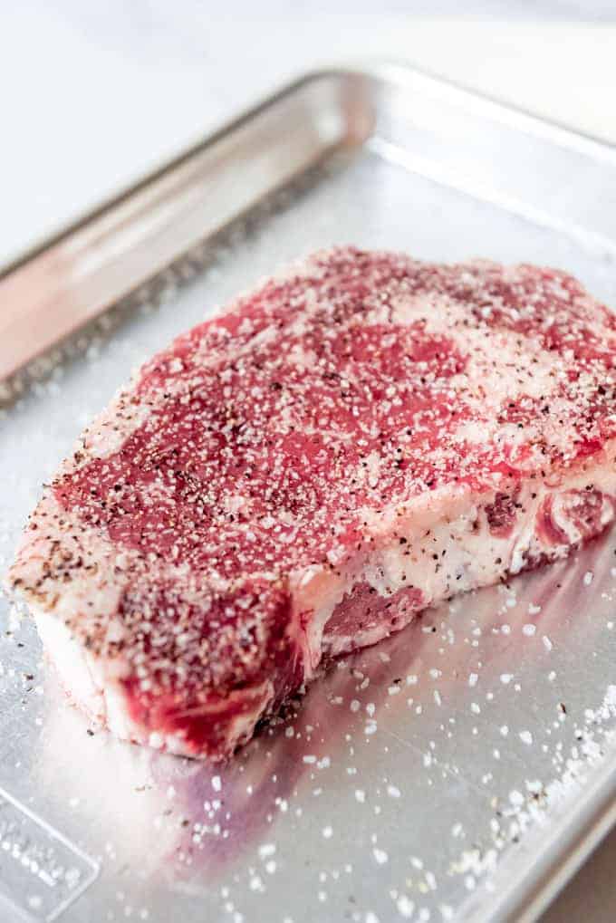 A seasoned ribeye steak on a baking sheet.