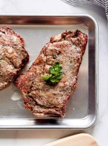 A grilled ribeye steak on a baking sheet with a parsley leaf on top.