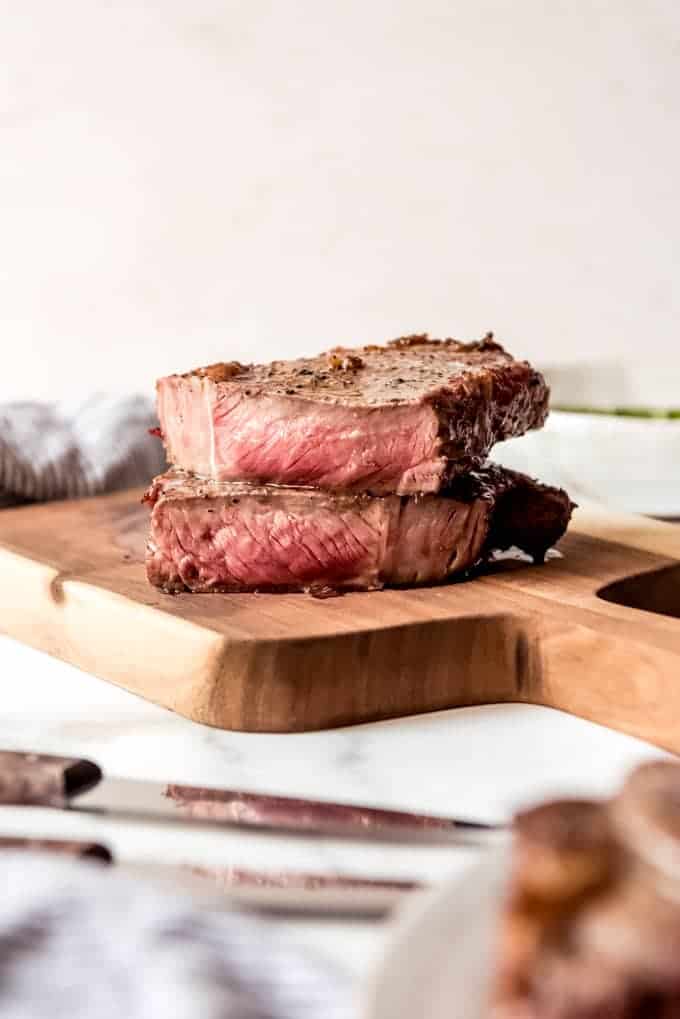 A grilled ribeye steak sliced in half on a wooden cutting board to show the warm red interior.