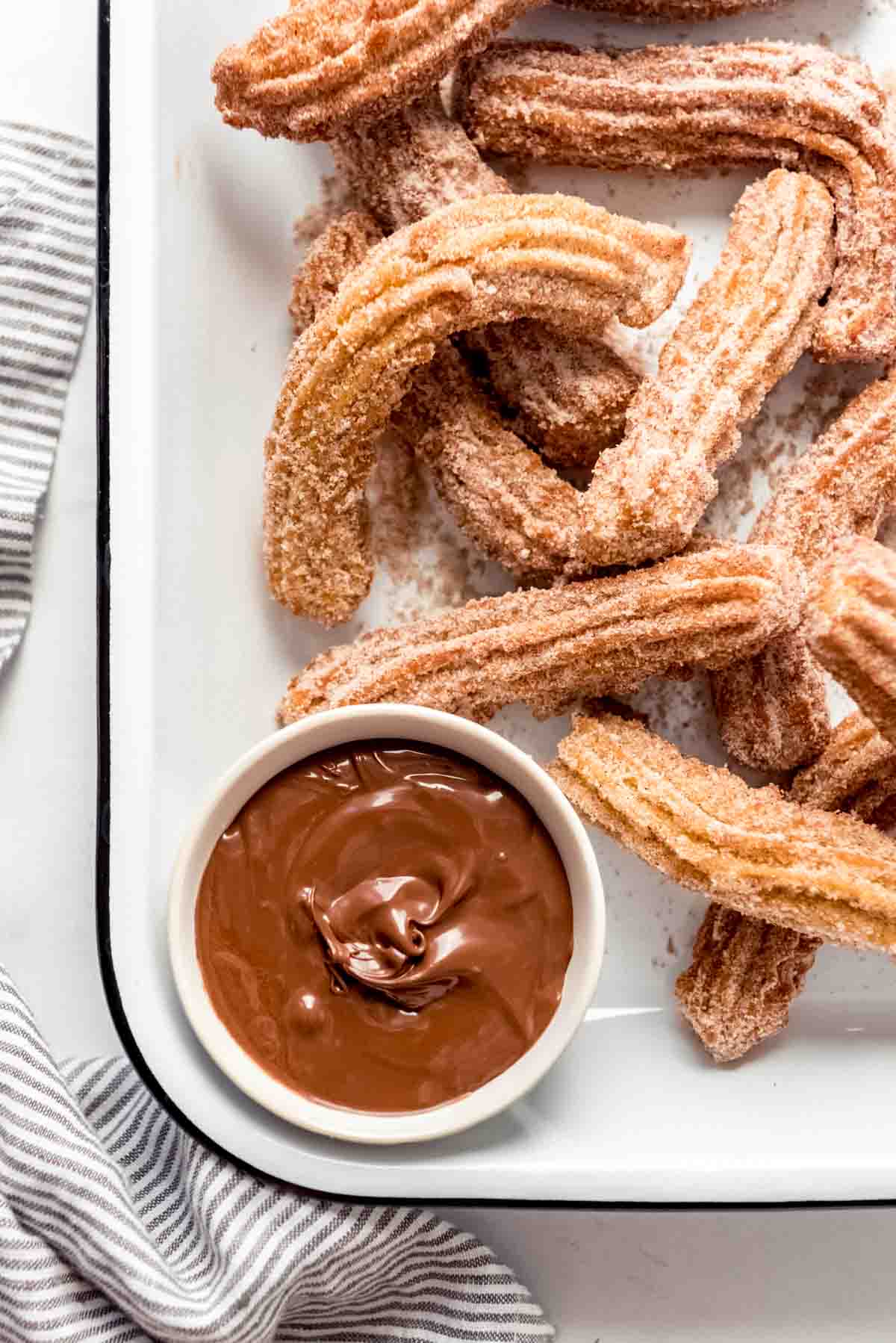 Homemade churros piled in a serving dish with Nutella for dipping.