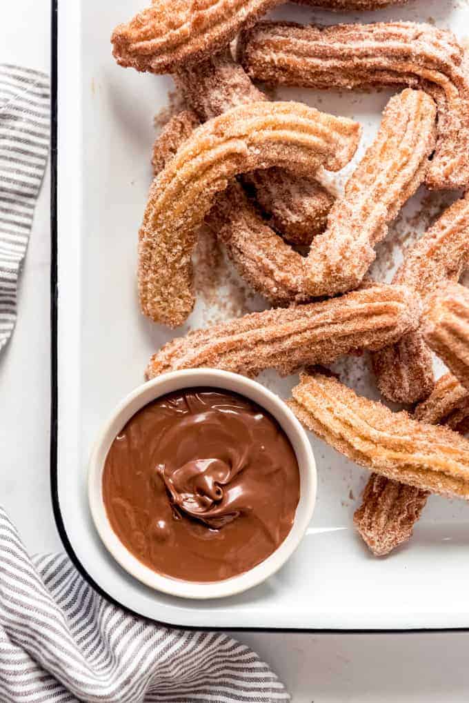 Homemade churros piled in a serving dish with Nutella for dipping.