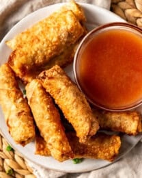 An overhead image of a plate of egg rolls with dipping sauce.