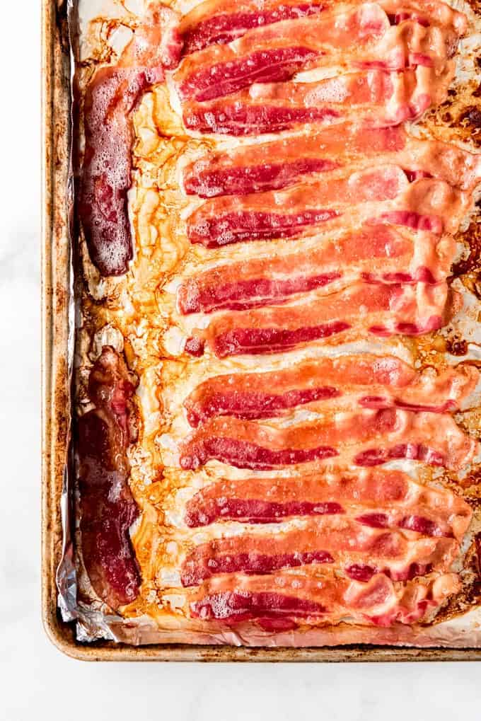 Slices of baked, thick-cut bacon on a foil-lined baking sheet.