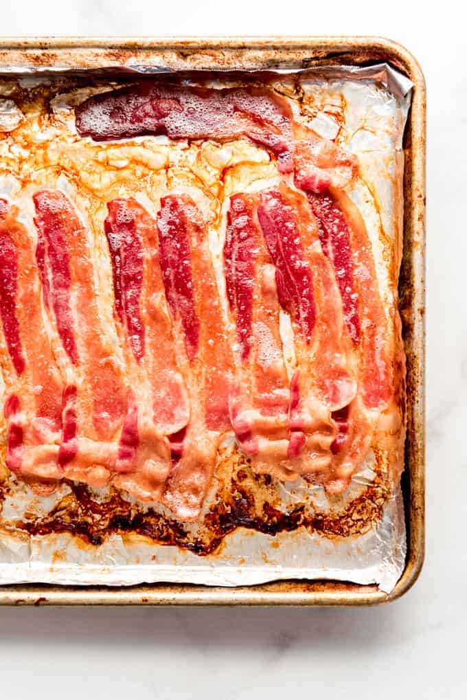 Cooked bacon in bacon grease on a baking sheet.