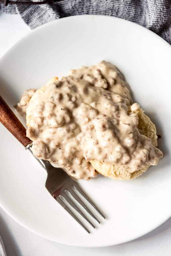 Buttermilk biscuits covered in homemade sausage gravy on a white plate with a fork.