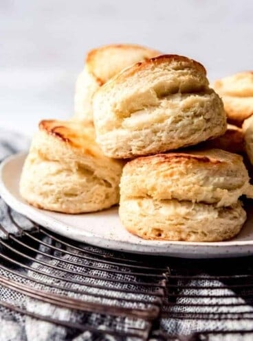 Buttermilk biscuits piled on a plate on a wire cooling rack on a towel